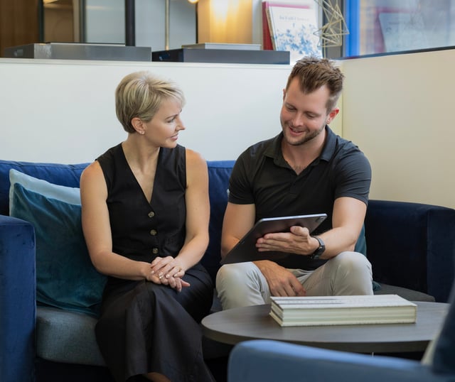 Two people seated on a blue sofa, looking at a tablet together.