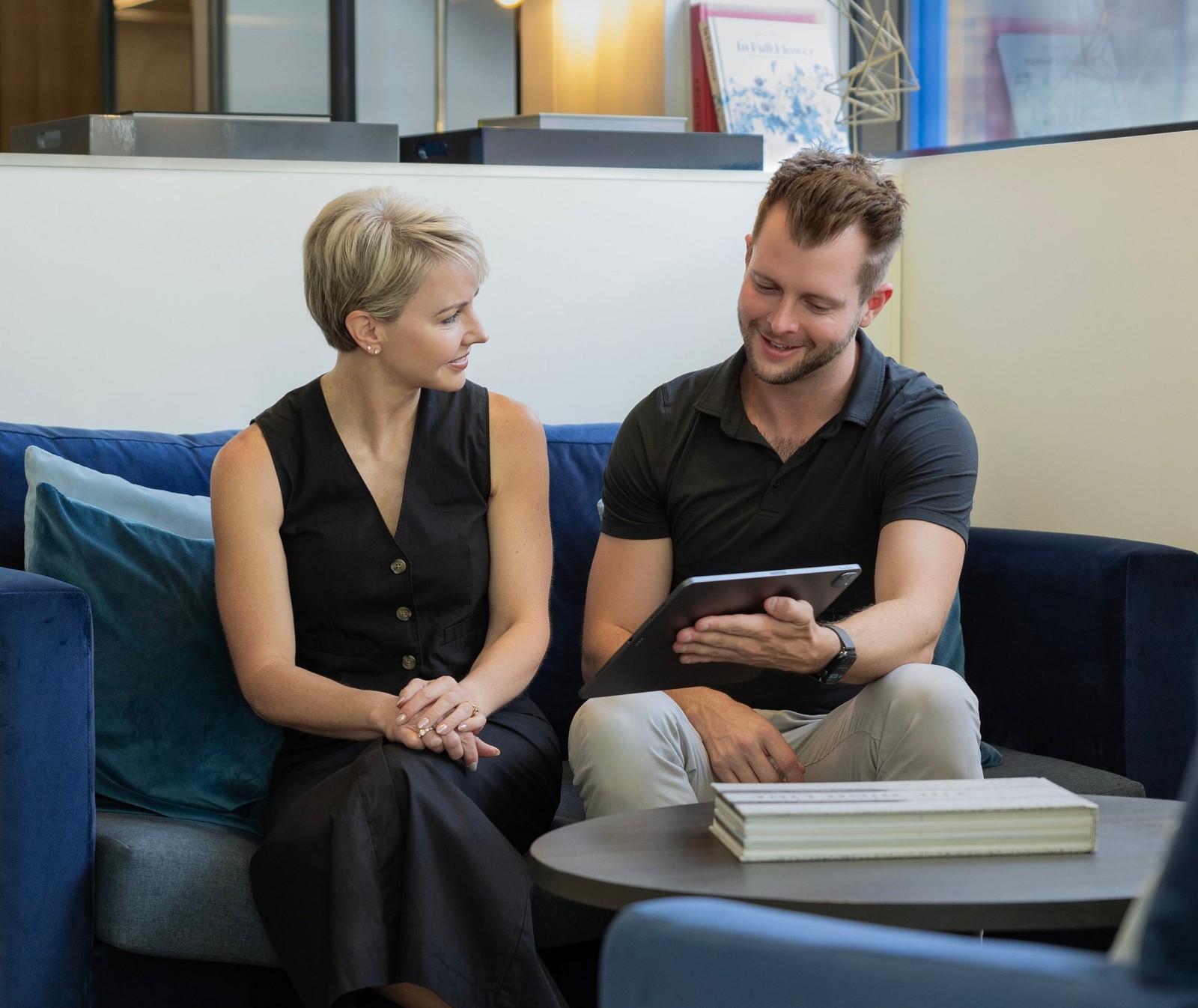 Two people seated on a blue sofa, looking at a tablet together.
